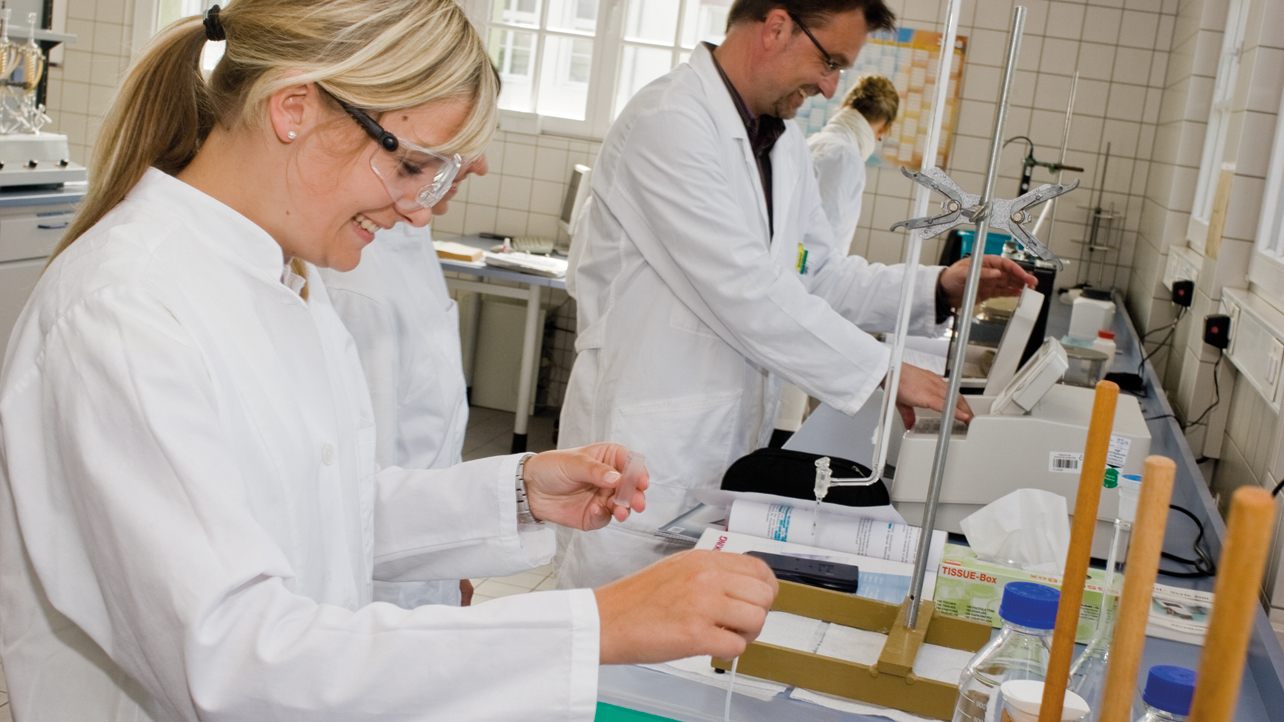 Professor und Studentin mit weißen Kitteln im Labor