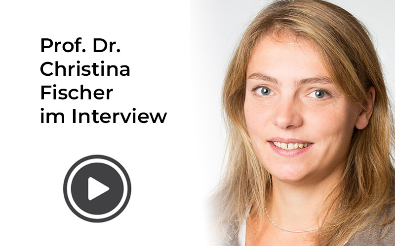 Porträt von Prof. Dr. Christina Fischer mit freundlichem Lächeln, die in einem Interview zu sehen ist. Abspielbutton deutet auf ein Video hin.