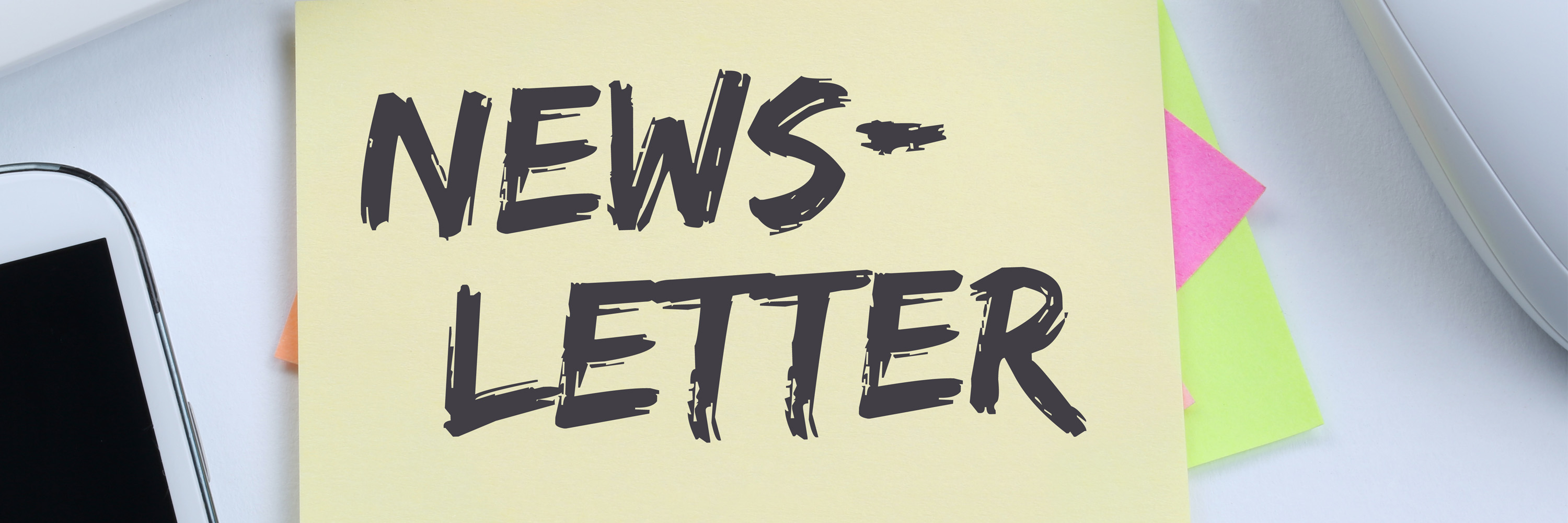 Gelbes Post-it mit handschriftlich geschriebenem, leicht schräg gehaltenem Text „NEWSLETTER“, daneben ein Handy und weitere bunte Notizzettel.