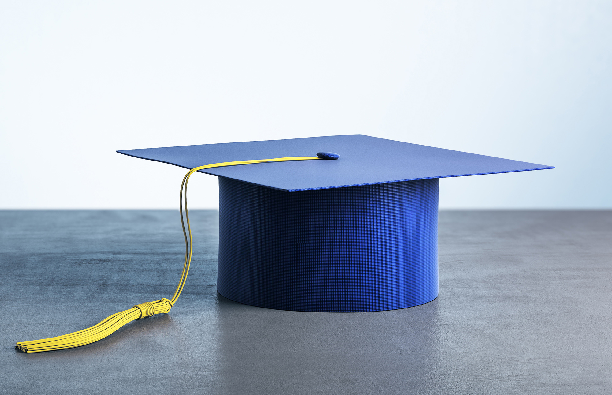 A dark blue graduation cap with a yellow tassel hanging from the right side, placed on a flat surface.