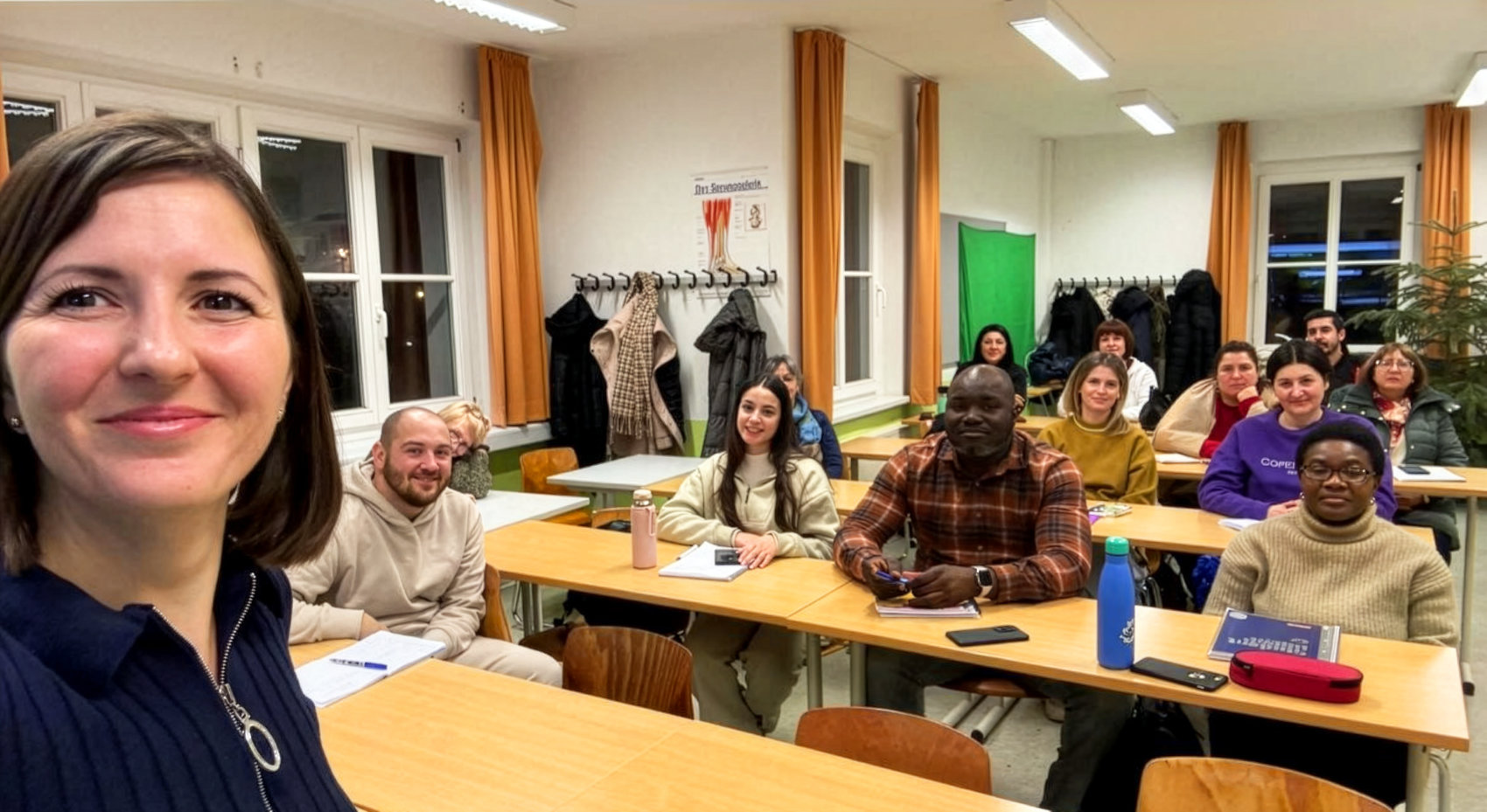 Eine lächelnde Frau im Vordergrund, daneben ein Gruppenfoto von etwa 15 Personen in einem hellen Klassenzimmer, die an Tischen sitzen und sich unterhalten. Die Atmosphäre wirkt freundlich und gesellig.