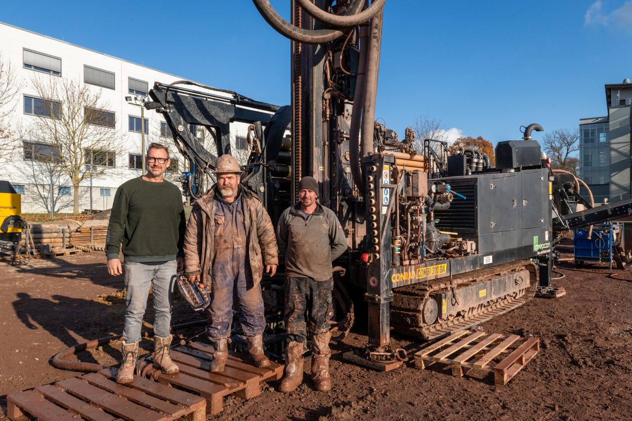 Drei Männer auf der Baustelle. Im Hintergrund ist der Bohrer zu sehen.