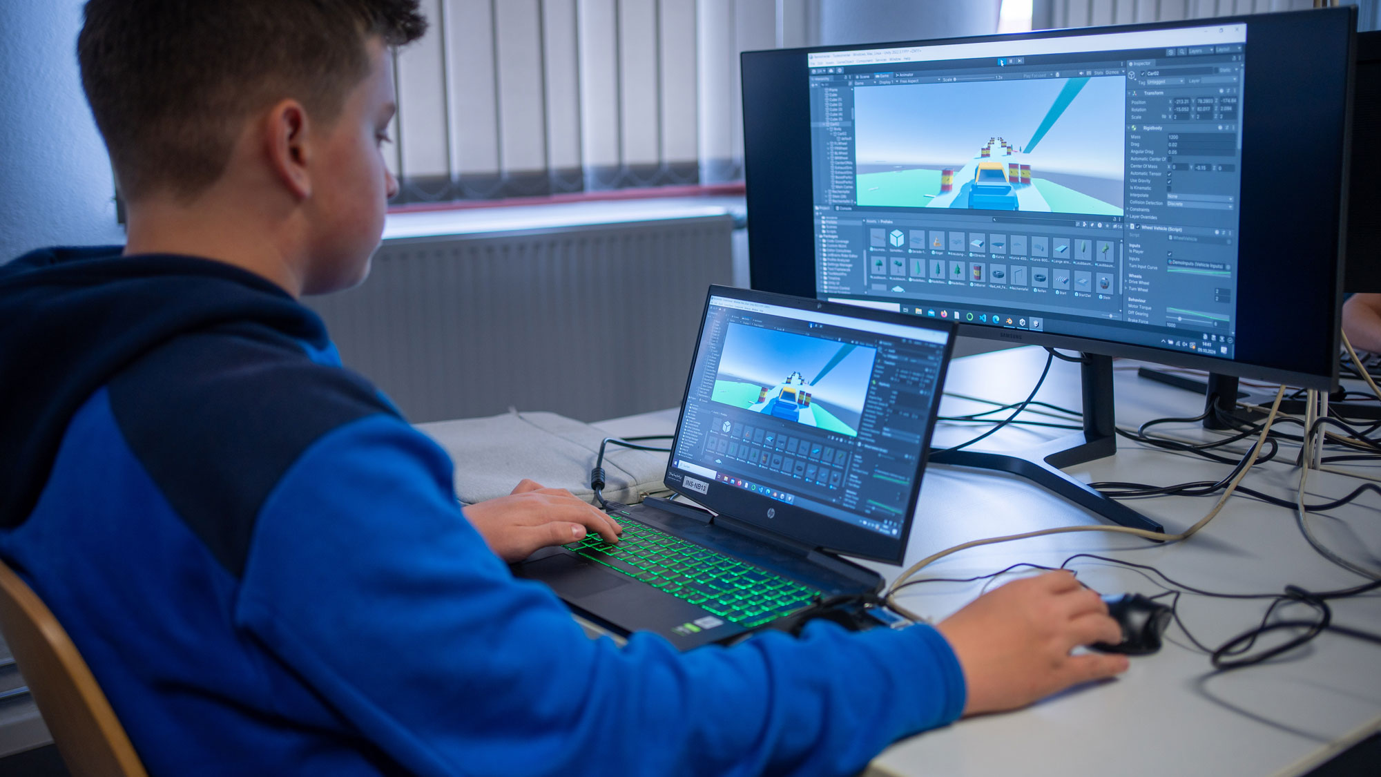 Eine Person arbeitet konzentriert an einem Schreibtisch mit zwei Bildschirmen und einem Laptop, auf denen 3D-Simulationssoftware mit einem Rennwagen-Modell zu sehen ist. Die Person bedient eine mechanische Tastatur und hält eine Maus in der Hand.