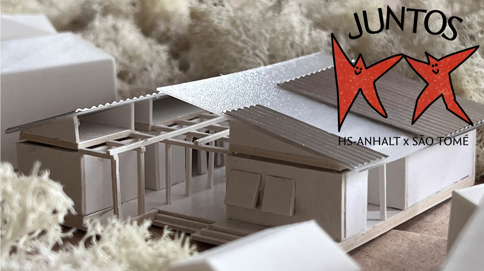 Modell eines modernen, flachen Gebäudes mit zwei markanten, roten Sternen-Symbolen, die das Logo des Projekts „Juntos“ darstellen. Das Gebäude ist Teil des Projekts „Pis Anhalt x São Tomé“.