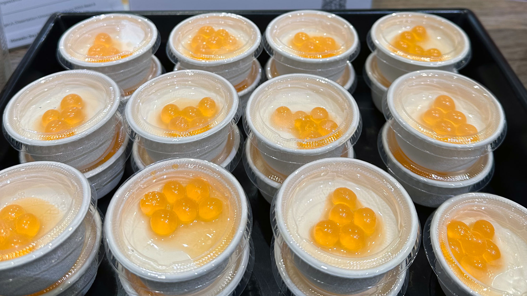 Mehrere kleine Gläser mit cremiger, weißlicher Dessertmasse, die mit drei Stückchen orangefarbenem, kandiertem Obst, vermutlich Orange oder Marmelade, garniert sind.