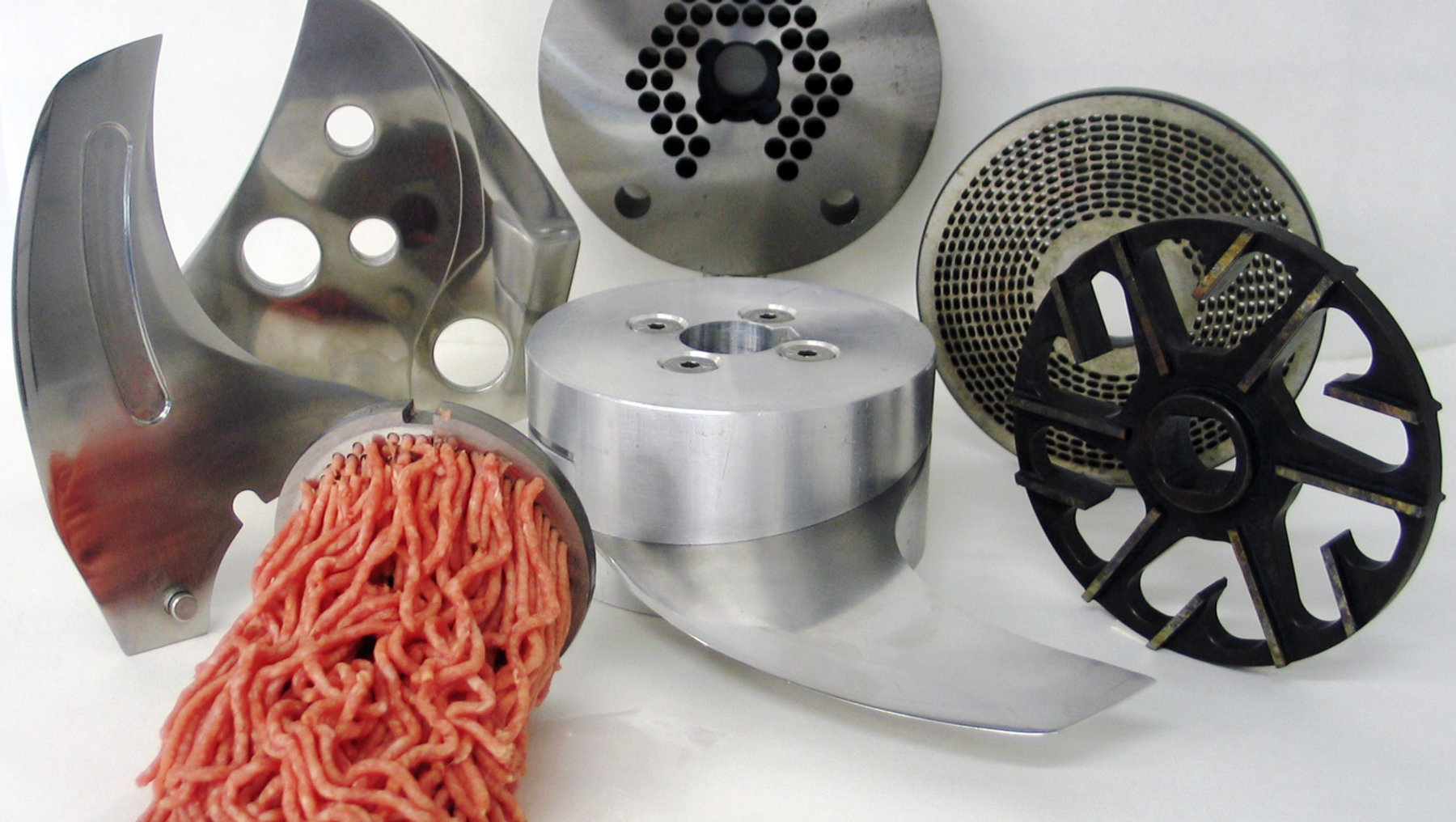 Dieses Bild zeigt verschiedene Metall-Pressformen für Hackfleisch und ähnliche Produkte, darunter diverse Scheiben und Rädchen mit unterschiedlichen Lochmustern sowie das daraus gepresste,drickige Hackfleisch im Block und als Spirale.
