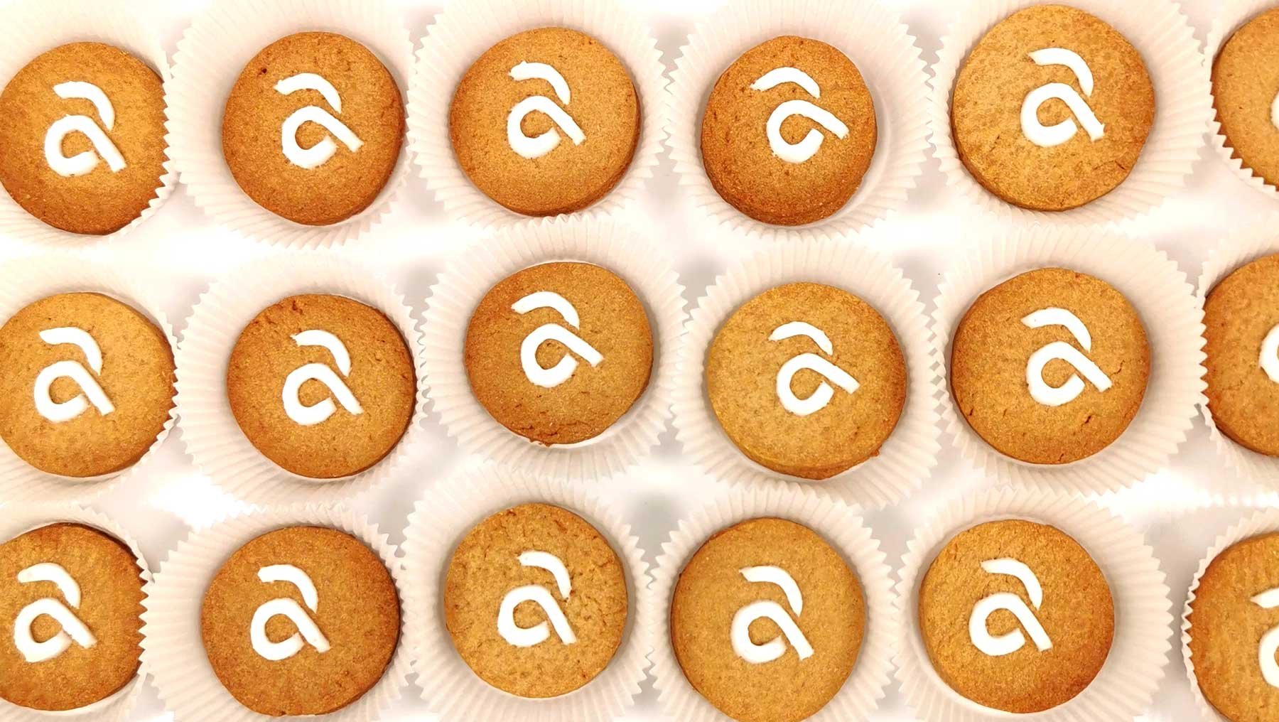 Zwölf gleichmäßig angeordnete Kekse mit goldbrauner Oberfläche, jeweils mit dem Logo der Hochschule Anhalt.