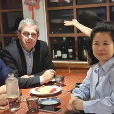 Vier Personen sitzen lächelnd an einem Tisch in einem Restaurant, umgeben von Tellern, Gläsern und Essensresten, während im Hintergrund Regale mit Flaschen zu sehen sind.