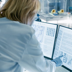 Zwei Laborassistenten in weißer Kleidung und Handschuhen analysieren genetische Daten auf einem Bildschirm mit DNA-Diagramm und Sequenzinformationen.