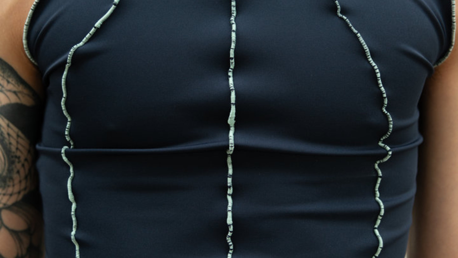 Diese Abbildung zeigt ein blackfarbenes Bustier mit hochgeschlossenem Halsausschnitt. Verziert ist es mit silberfarbenen, gewellten Stickereien, die den Bustier in der Mitte und an den Seiten schmücken. Das Stück scheint aus stretchigem Material zu sein.