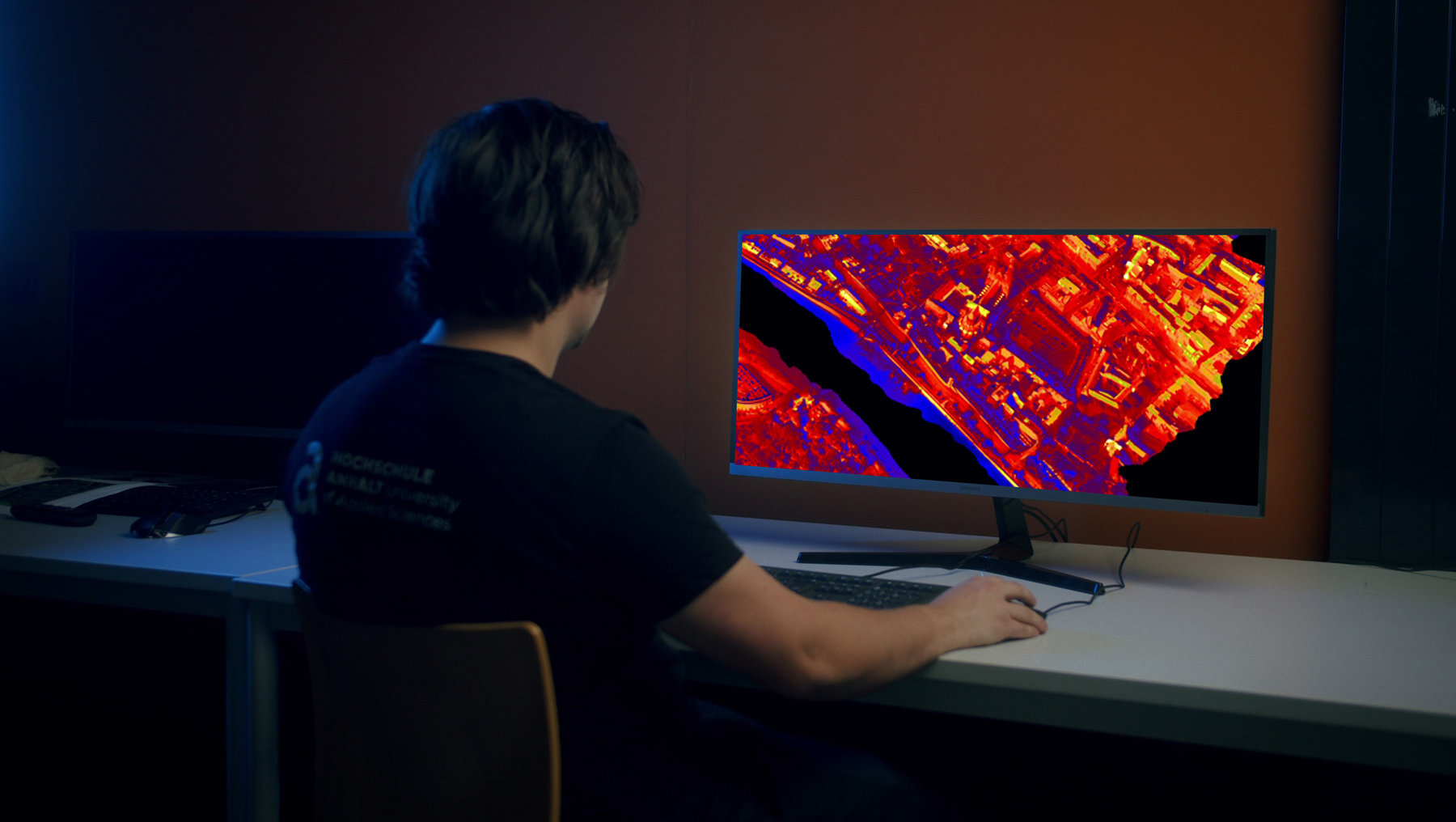 Symbolbild Fernerkundung 3D Thermographie zeigt Person am Bildschirm mit rote-gelben Wärmebildaufnahmen einer Stadt