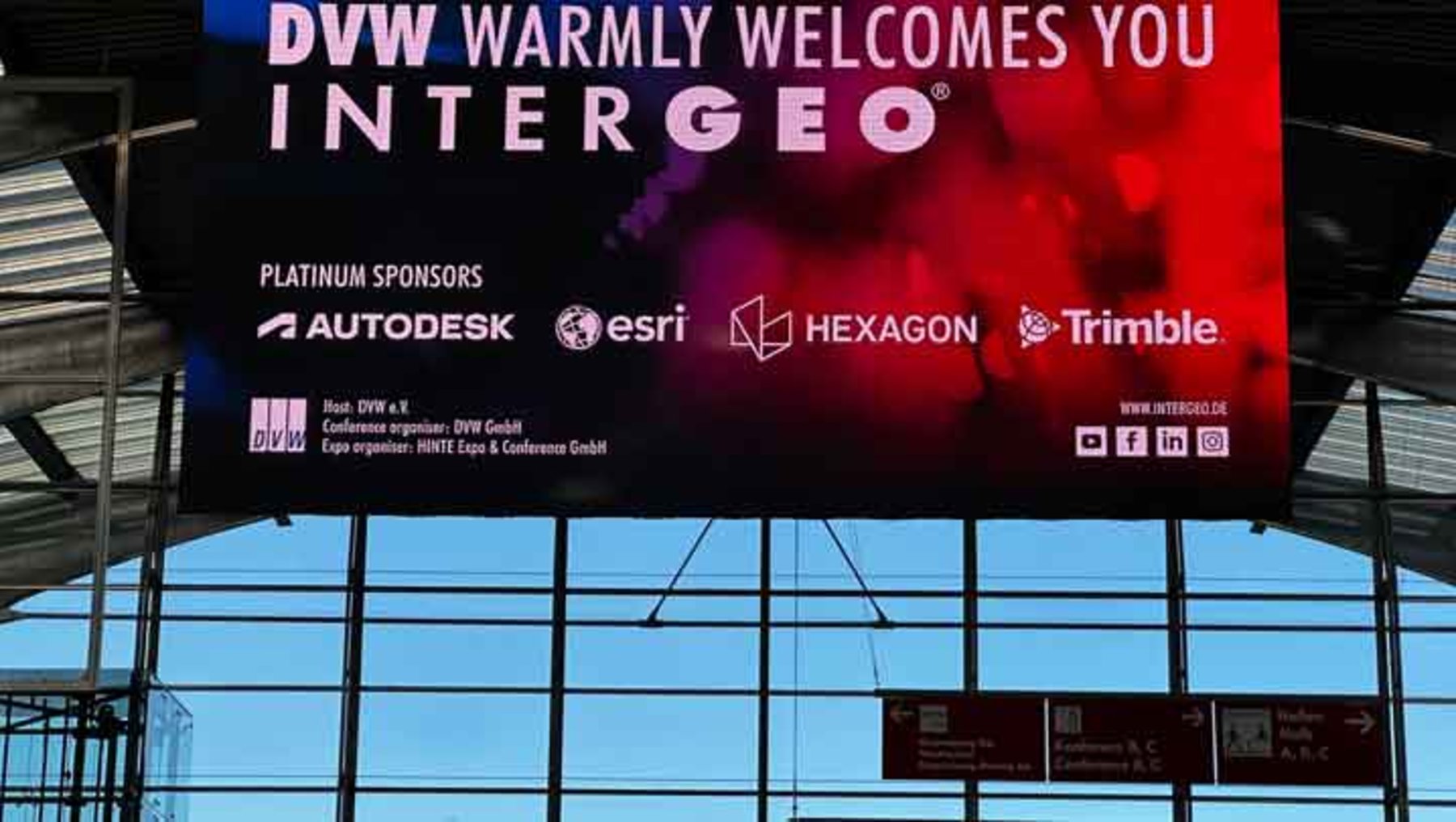 Großes Willkommensbanner der DVW zur Intergeo mit dem Schriftzug „DVW warmly welcomes you Intergeo“. Darunter sind die Logos der Platin-Sponsoren Autodesk, Esri, Hexagon und Trimble abgebildet.