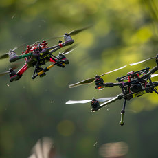 Zwei Drohnen fliegen im Freien, eine mit farbiger, dekorativer Struktur und vier Rotoren, die andere technisch mit Kamera und vier Propellern.