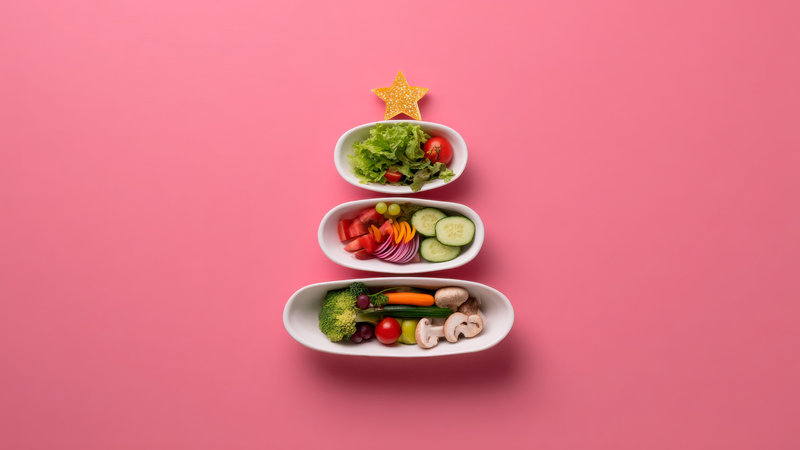 Drei Schalen mit Gemüse bilden eine Pyramide mit einem Stern obenauf. Die unterste Schale enthält Brokkoli, Karotten, Tomaten und Pilze, die mittlere Gurken, Paprika und Tomaten, die oberste Salat mit Tomaten.