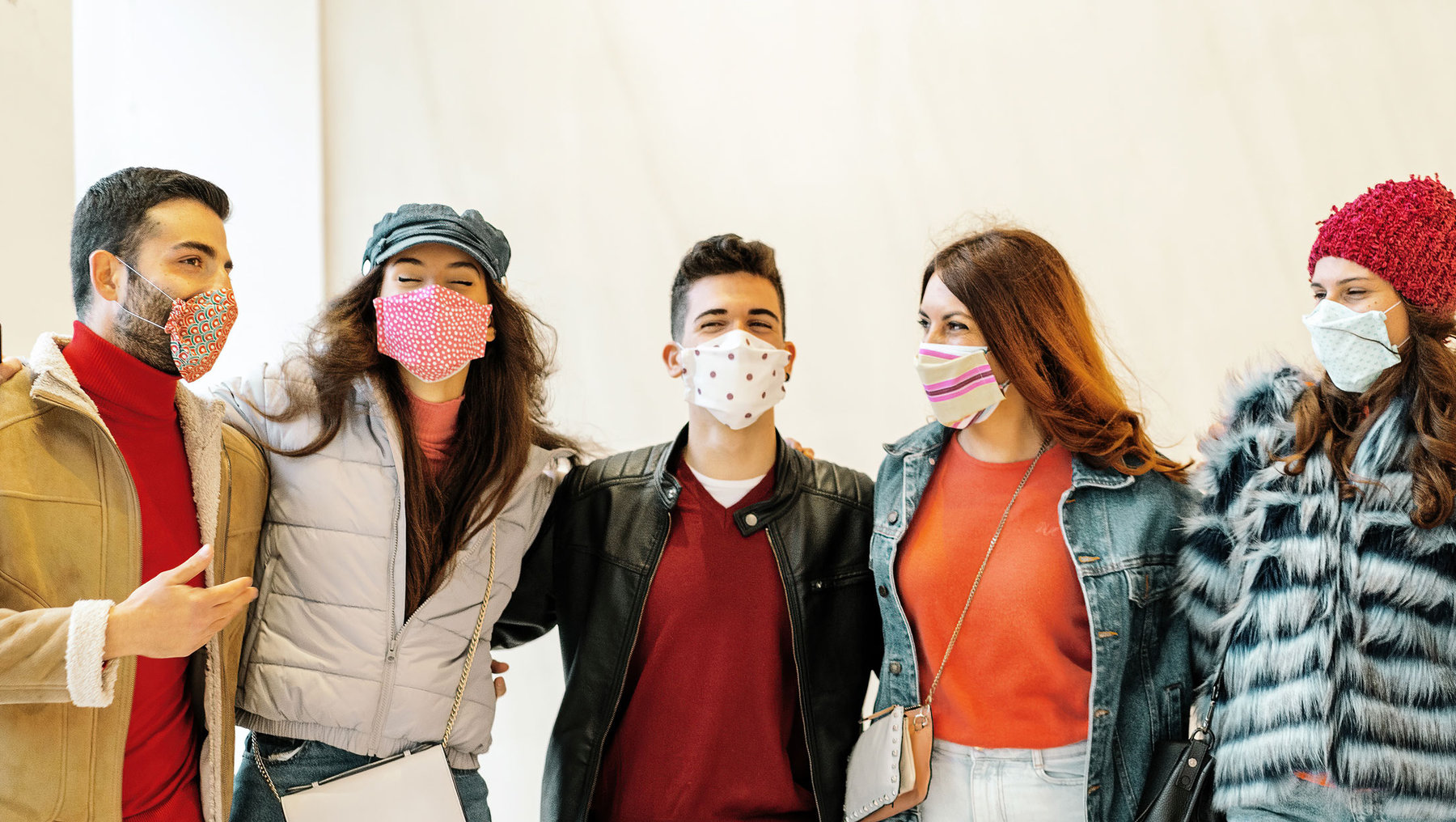 Eine Gruppe von fünf Personen steht nebeneinander und trägt Gesichtsmasken. Sie lächeln und wirken fröhlich. Die Personen sind warm gekleidet, einige tragen Jacken und Mützen. Die Szene wirkt freundschaftlich und gesellig.