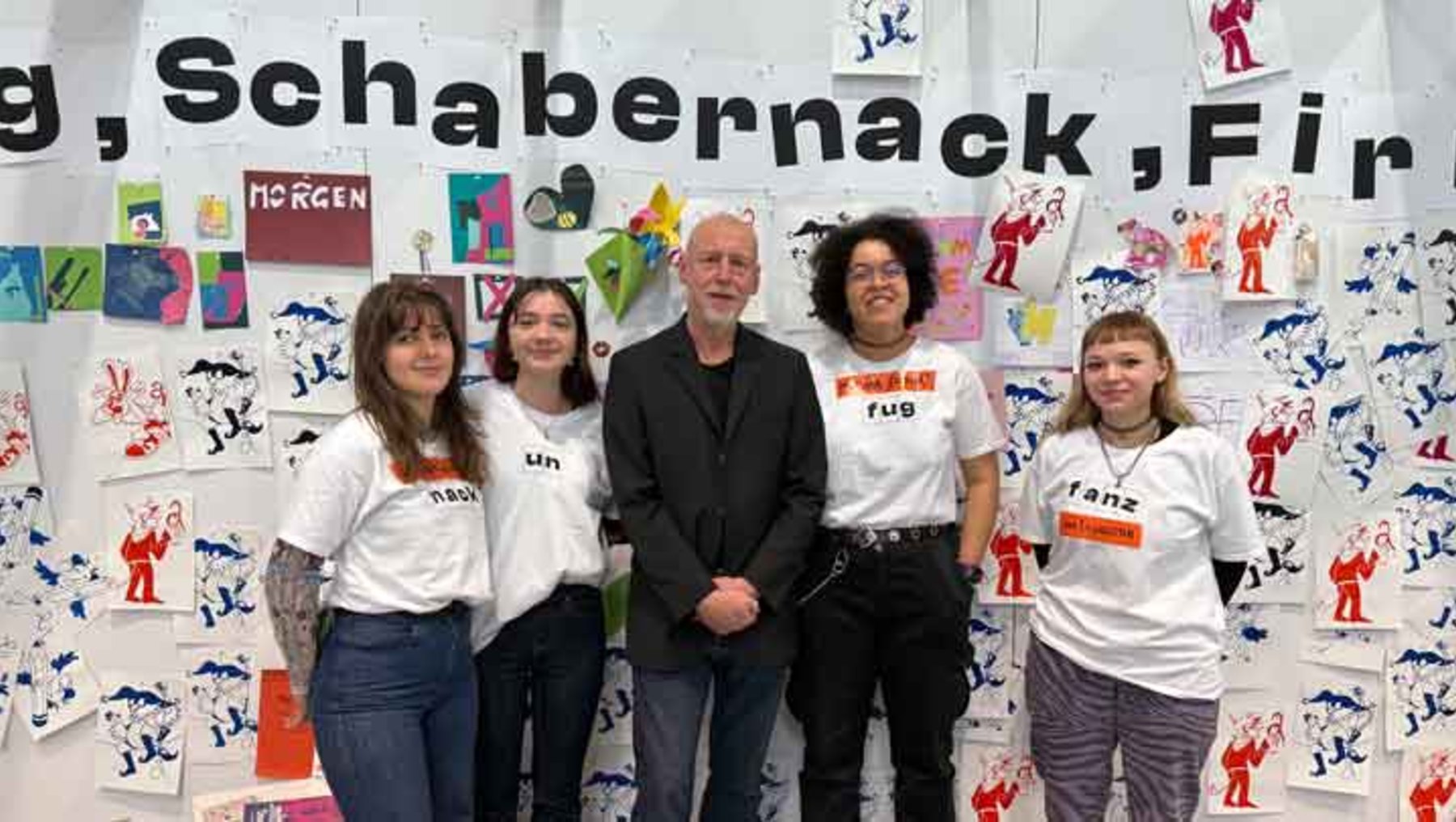 Fünf Personen stehen lächelnd vor einer bunten Collage mit kindlichen Zeichnungen von Menschen in verschiedenen Posen. Sie tragen weiße T-Shirts mit Aufdrucken wie „Fridays for Future“ und „last generation“. Über ihnen steht der Schriftzug „Fridays for Future, Schabernack, Firn“.