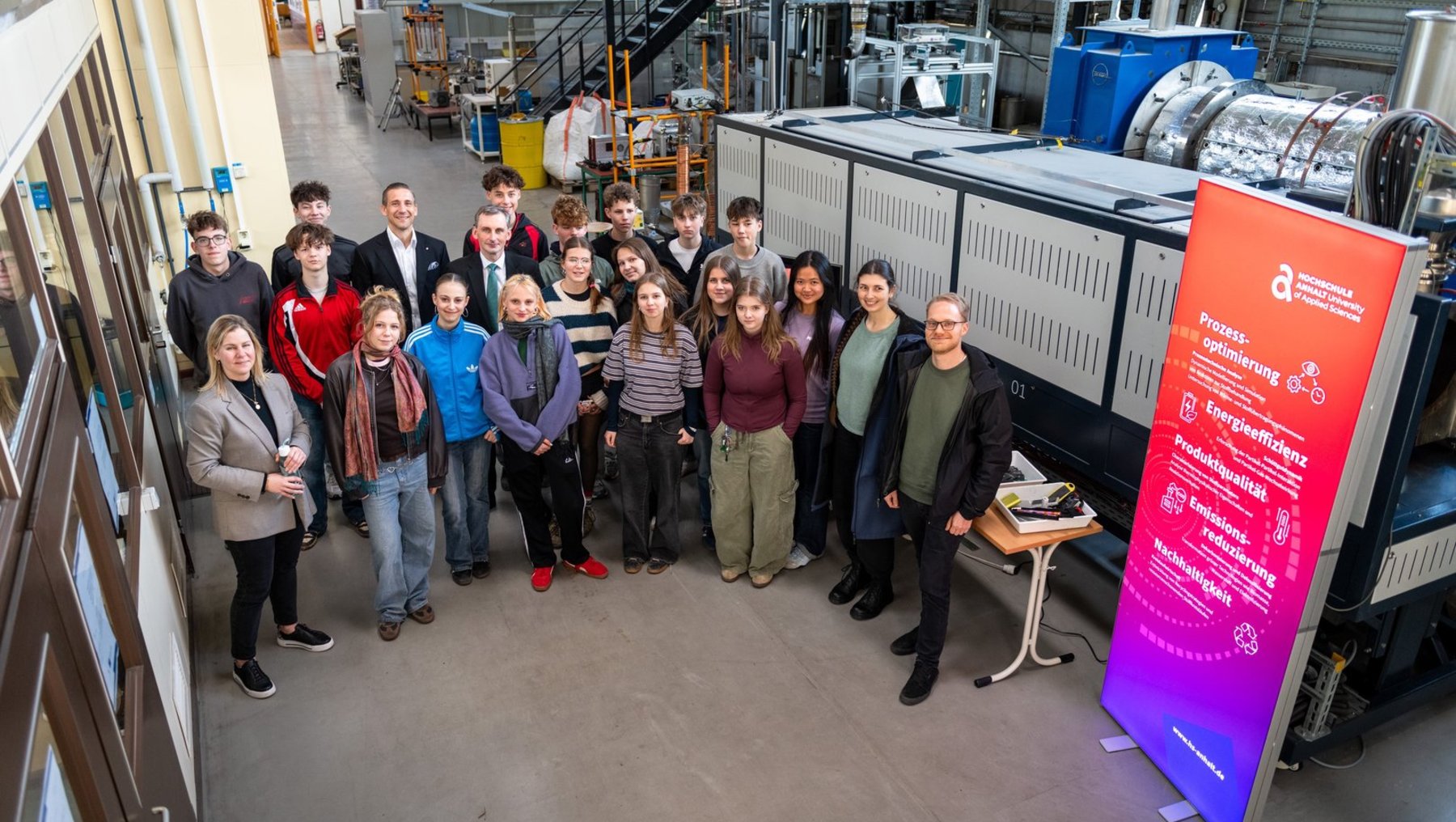 Gruppe von etwa 20 Personen steht lächelnd vor einem großen technischen Gerät, vermutlich einer Maschine oder Anlage, in einem Industrieumfeld. Dahinter sind Werkzeuge und Maschinen zu sehen. Rechts steht ein Banner mit dem Schriftzug „Festo Engineering“.