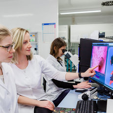 Studierende in weißen Kitteln vorm Computer