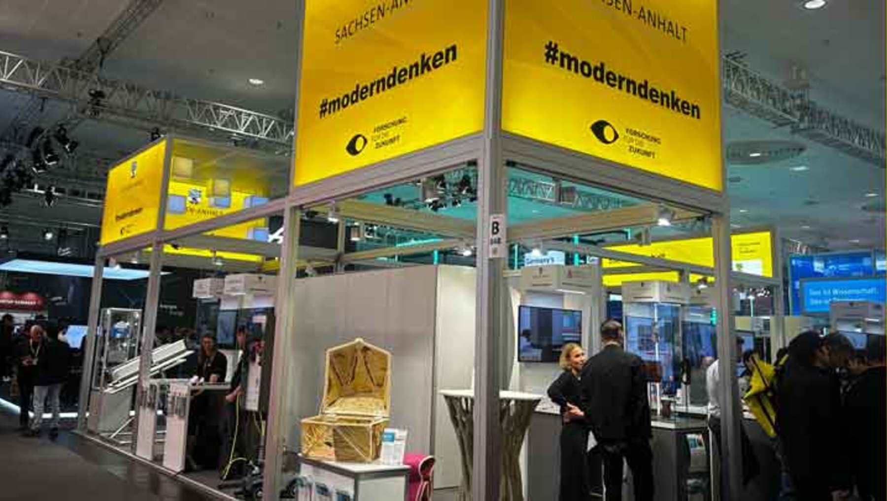 Großer Messestand mit gelben Wänden und Aufschrift „#moderndenken“ sowie „Sachsen-Anhalt“. Im Hintergrund Besucher, die sich an Infotischen und Displays informieren.