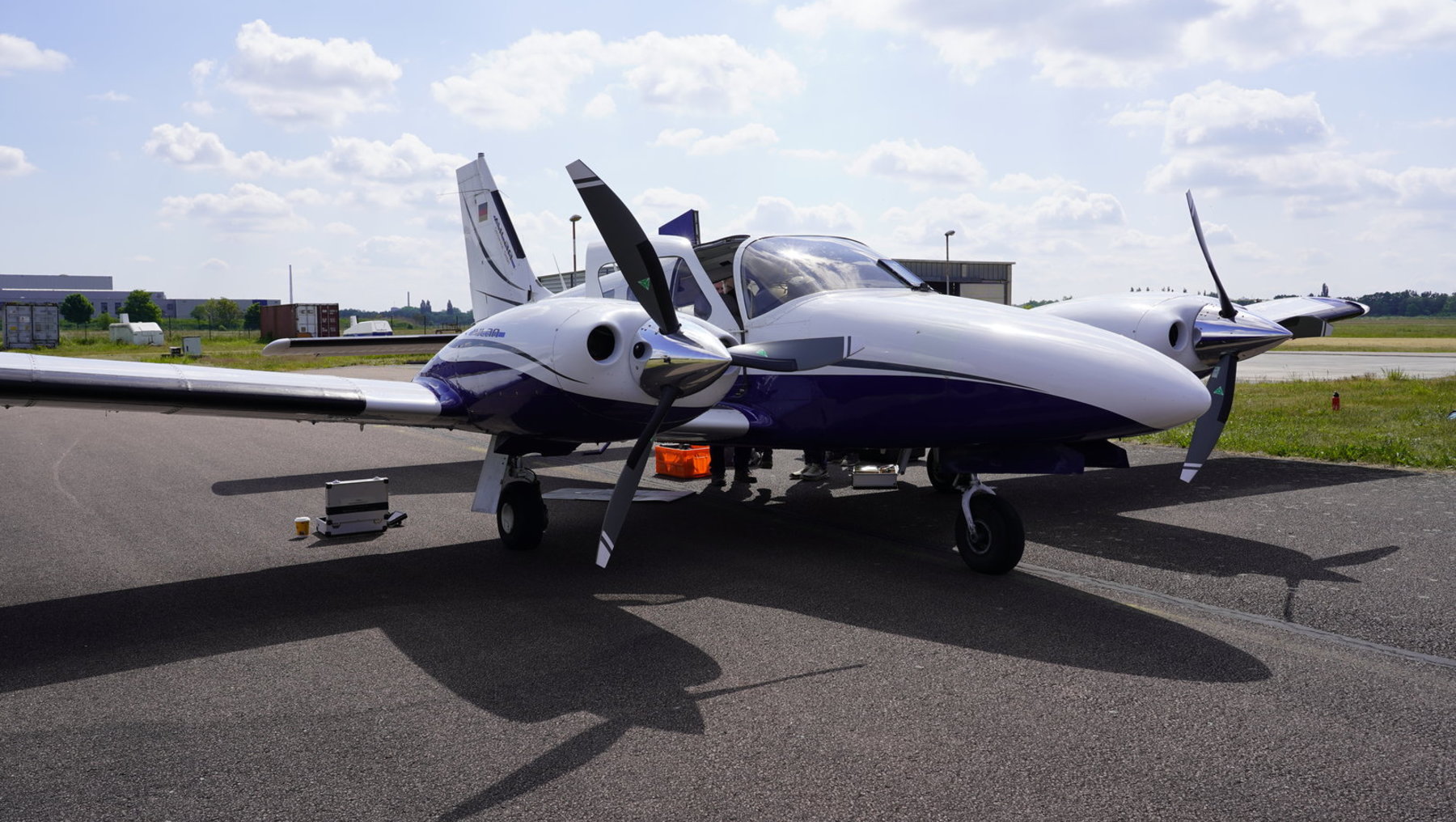 Diese Abbildung zeigt ein kleines Leichtflugzeug mit einem einmotorigen Propeller, das auf einem Asphaltplatz steht. Das Flugzeug besitzt eine silberne und bläue Farbgebung mit einigen Kennzeichnungen.