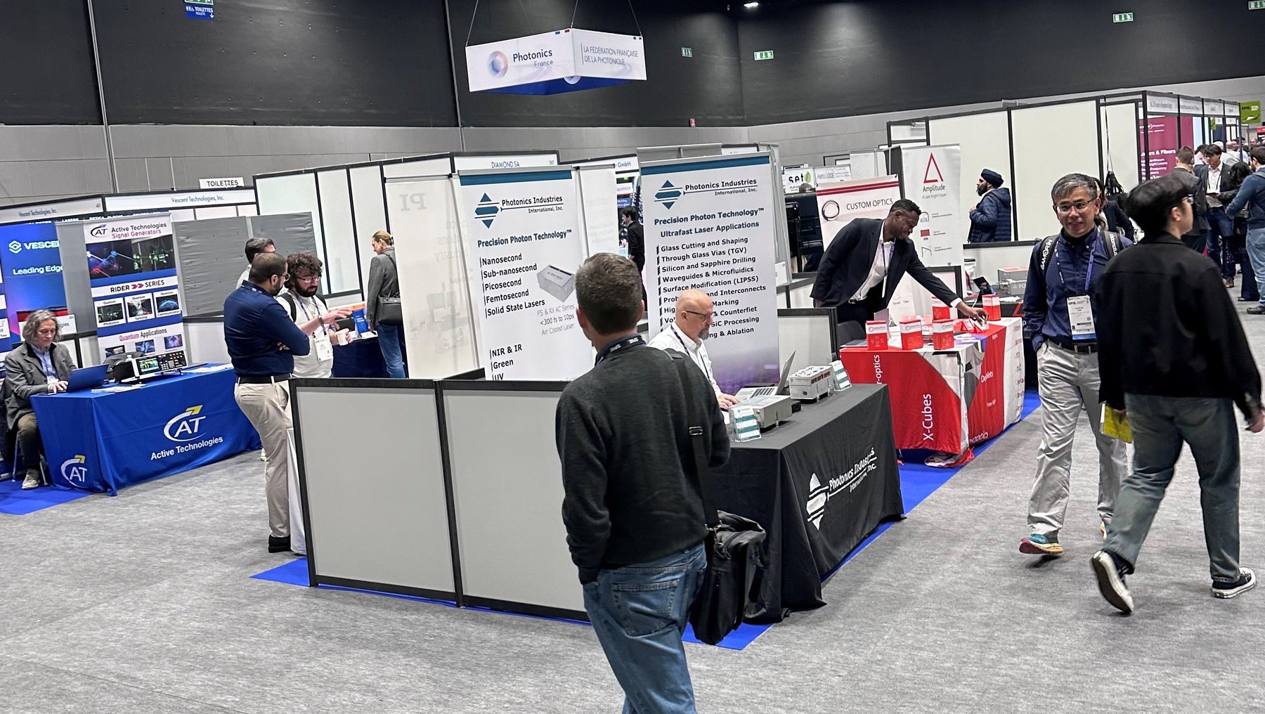 Messe mit mehreren Ausstellungsständen, an denen Besucher mit Ausstellern sprechen. Ein Mann steht vor einem Infotisch mit Plakaten und Flyern zu Themen wie Patientensicherheit und Medizintechnik. Im Hintergrund weitere Stände mit Fachpersonal und Interessenten.
