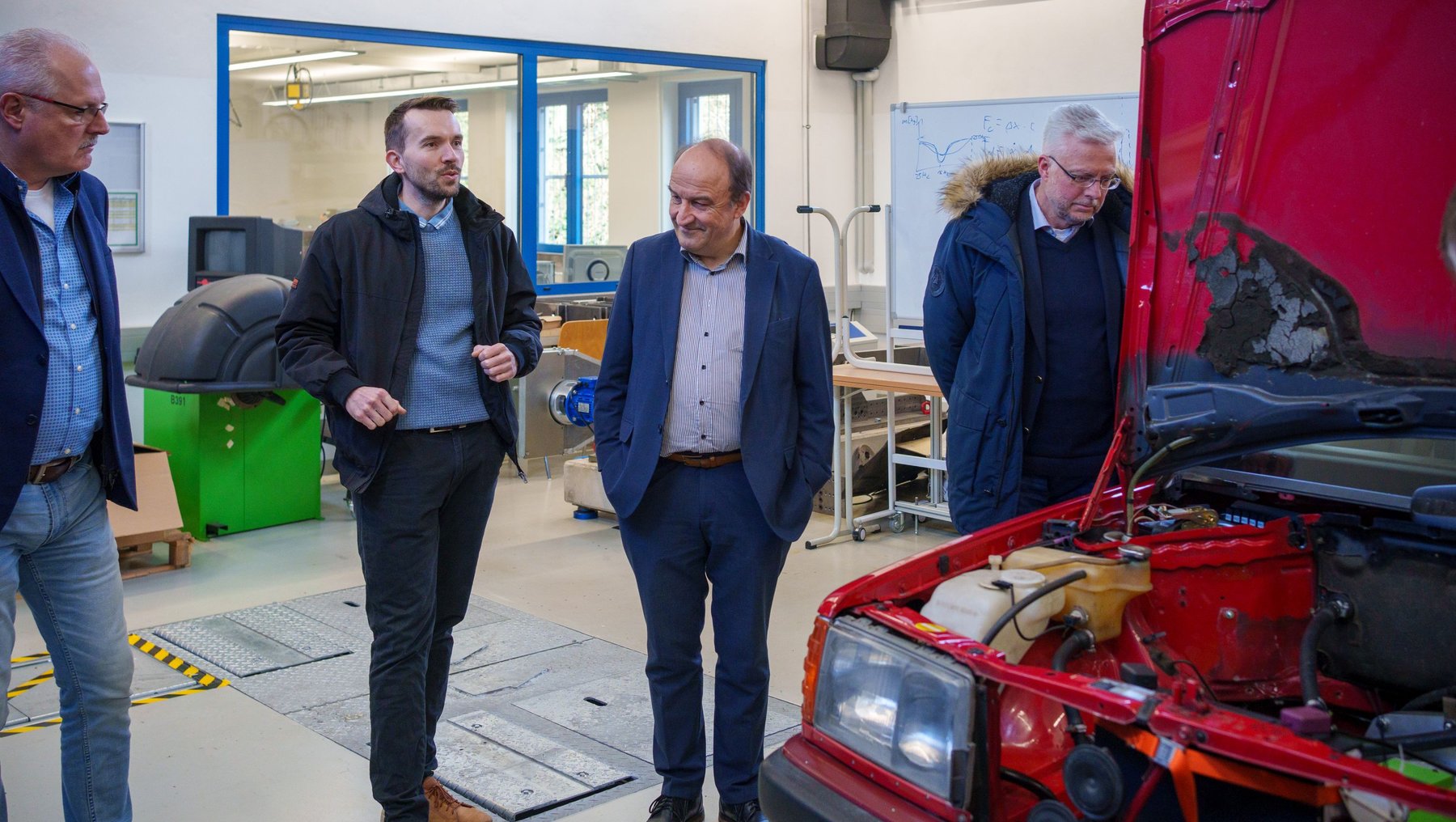 Vier Teilnehmer der VDI-Tagung im Technikum Fahrzeugtechnik: Ein rotes Auto mit offenem Motorraum wird besichtigt, während die anderen drei Personen interessiert zuschauen und sich unterhalten.
