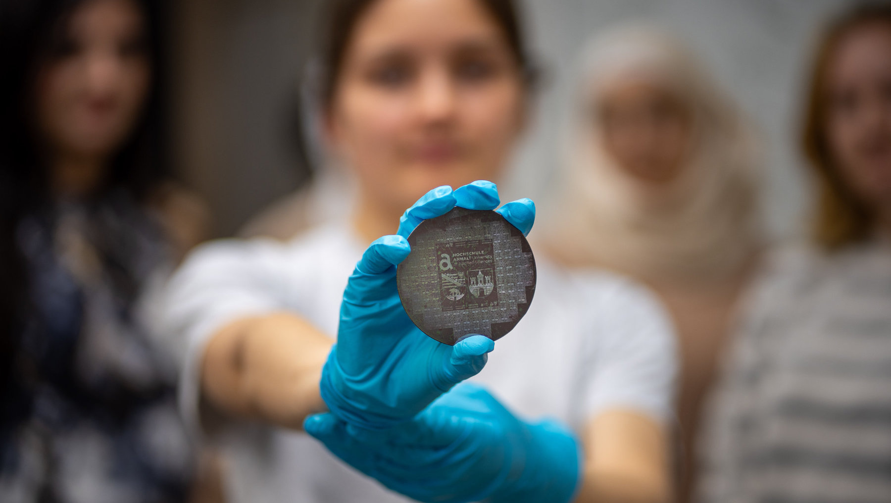 Eine Gruppe von Studentinnen im Praktikum (im Hintergrund) mit einem Halbleiter Wafer (im Vordergrund)