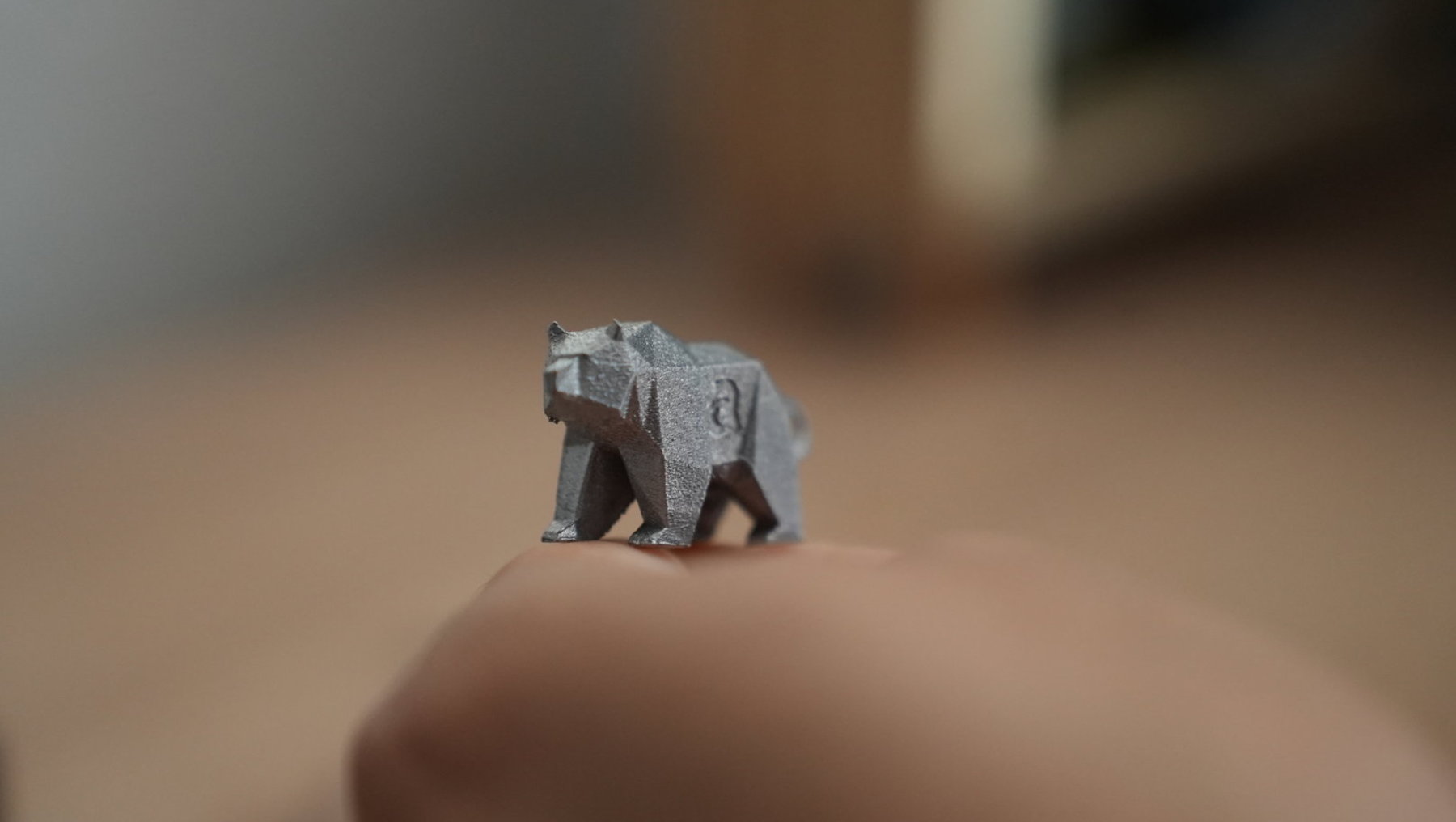 Ein Origami-Bär aus dunklem Papier sitzt auf einer Handfläche und blickt nach vorne.