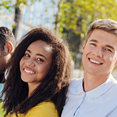 Four happy people outdoors, smiling and looking at a map together, suggesting teamwork and exploration in a bright, sunny environment.