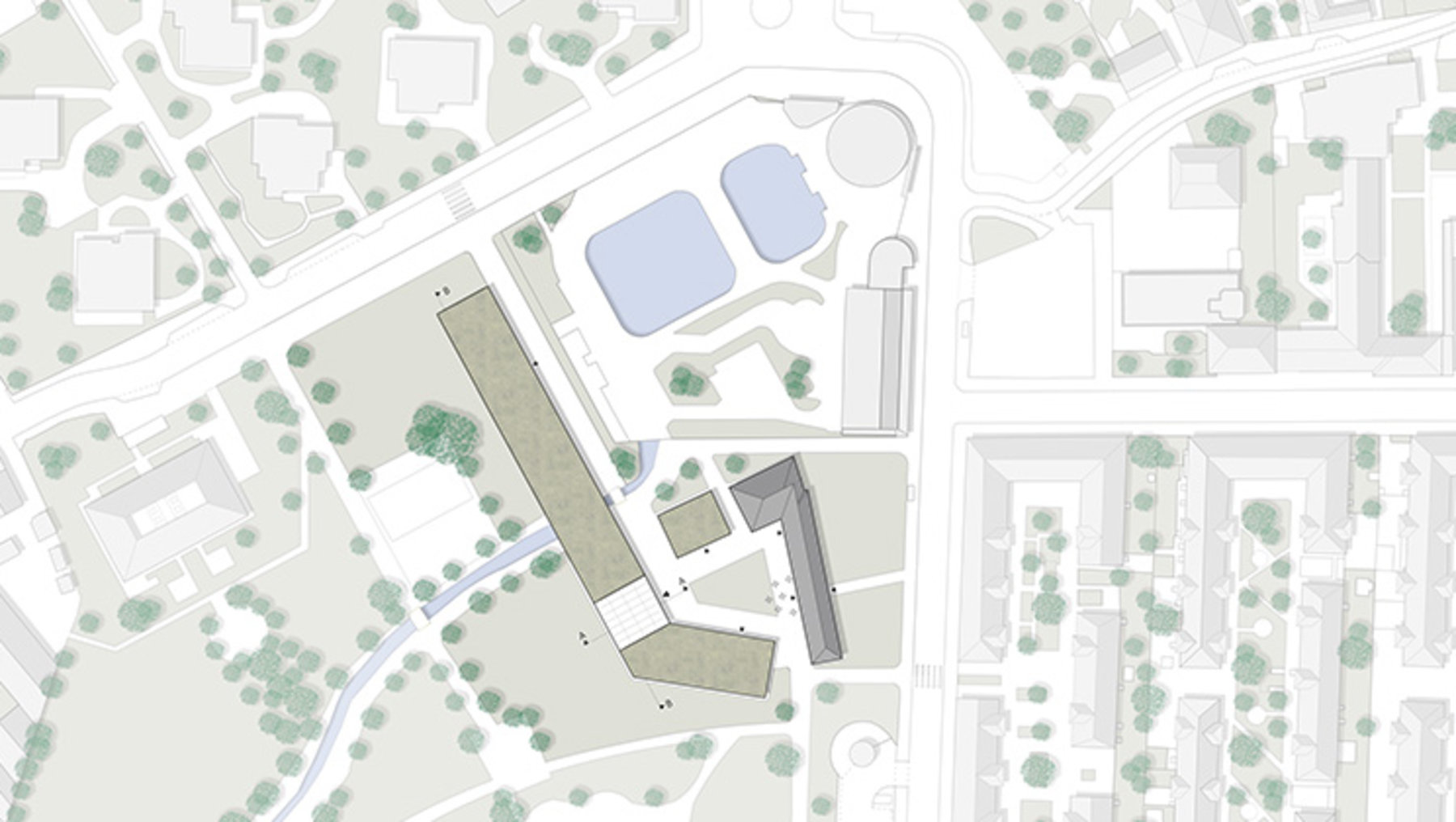 Luftbild eines Schul- oder Bildungskomplexes mit zentralem, länglichem Hauptgebäude, zwei kleineren Anbauten und einem Sportplatz mit zwei Becken sowie angrenzenden Grünflächen und Wegen.
