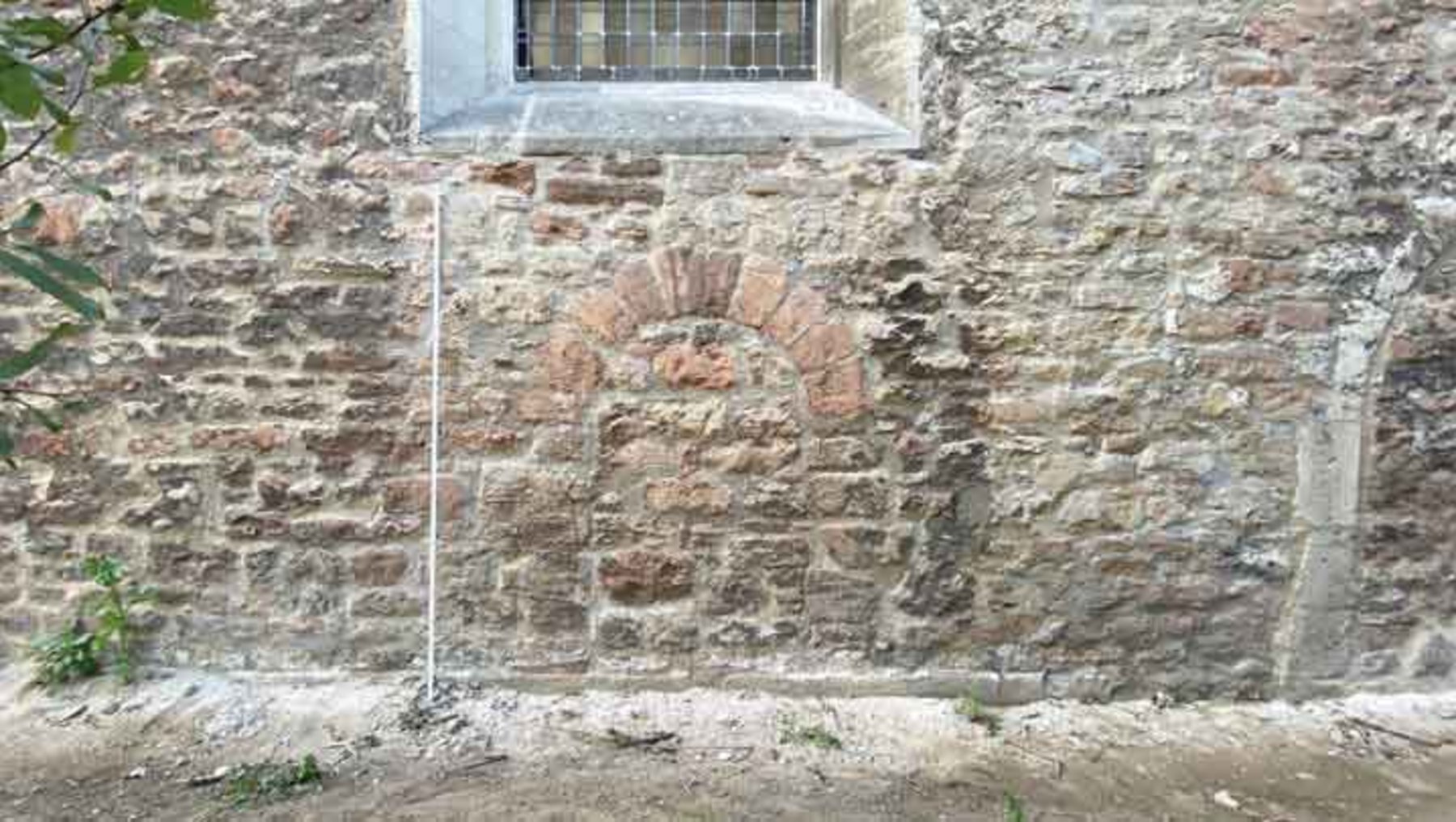 Alter Steinmauerabschnitt mit eingelassenem, kreisförmigem Relief aus hellem Stein, das ein stilisiertes, nach oben geöffnetes Herz mit verzierten Rändern zeigt.