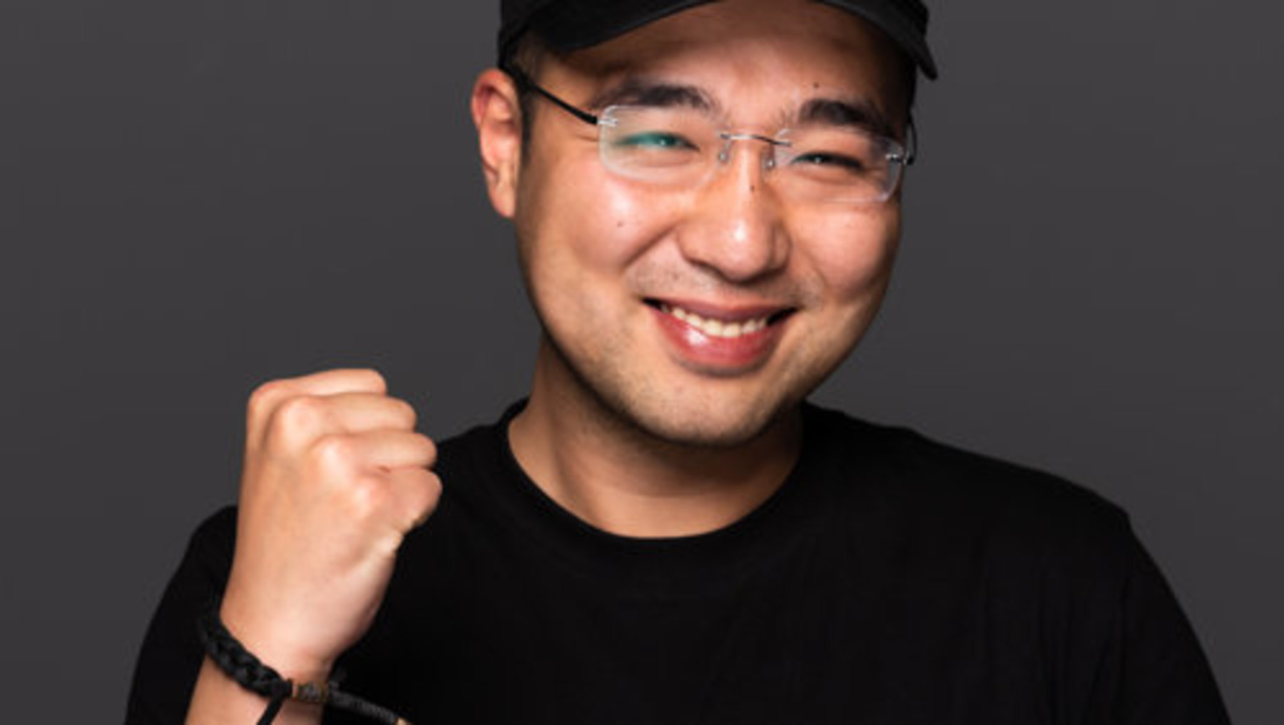 Lächelnder Mann mit Brille und schwarzer Basecap, der mit geballter Faust nach oben zeigt, trägt ein schwarzes T-Shirt mit dem Aufdruck „Richmond“.