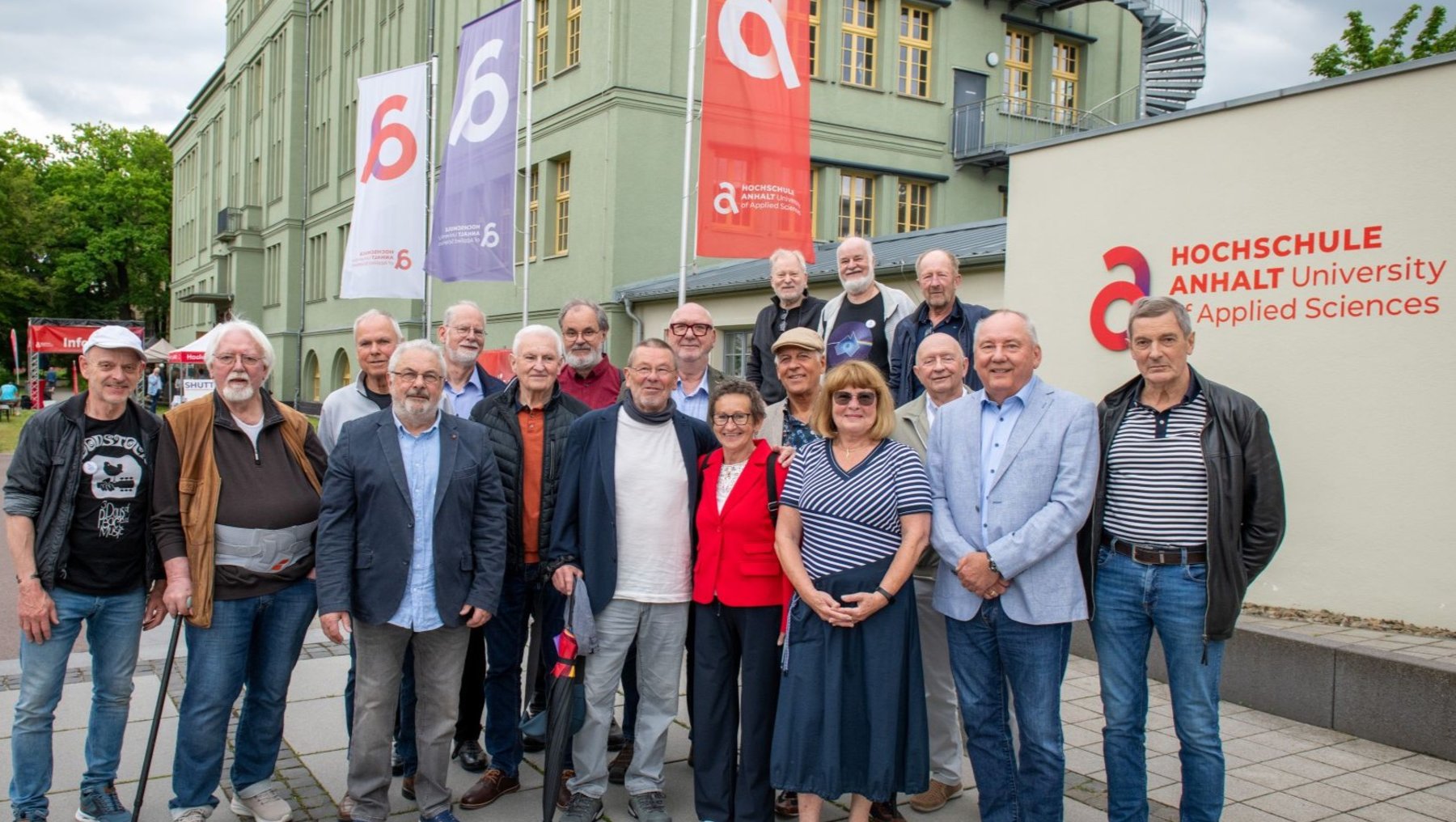 Gruppe von etwa 15 älteren Personen, die vor einem Gebäude der **Hochschule Anhalt – University of Applied Sciences** stehen, lächelnd für ein Gruppenfoto. Im Hintergrund Banner mit Logo.