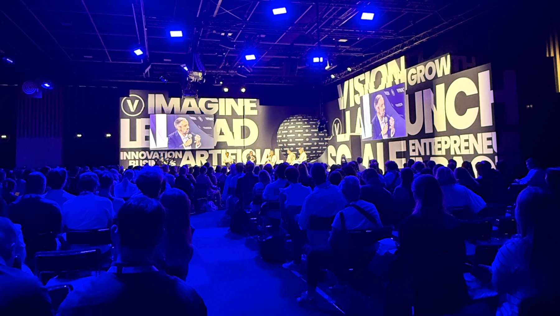 Großer Kongresssaal mit Publikum, in dem auf einer großen Leinwand die Worte „Imagine LA, Vision Grow, Launch, Innovation Artificial Intelligence, Social Entreprene“ in hellen Buchstaben projiziert werden.