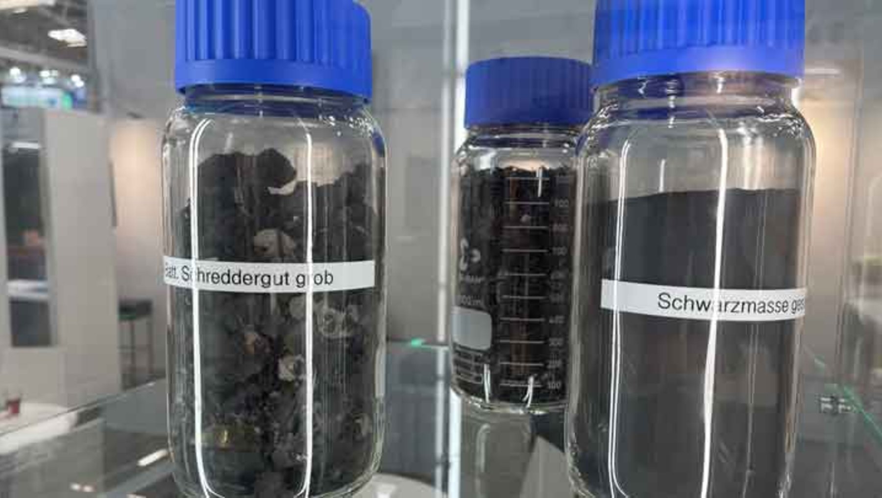 Zwei durchsichtige Gläser mit blauen Deckeln, die jeweils mit getrockneten Pflanzenresten gefüllt sind. Beschriftet mit „getrocknete S. hreddergut glob“ und „Schwärzmasse prob“.