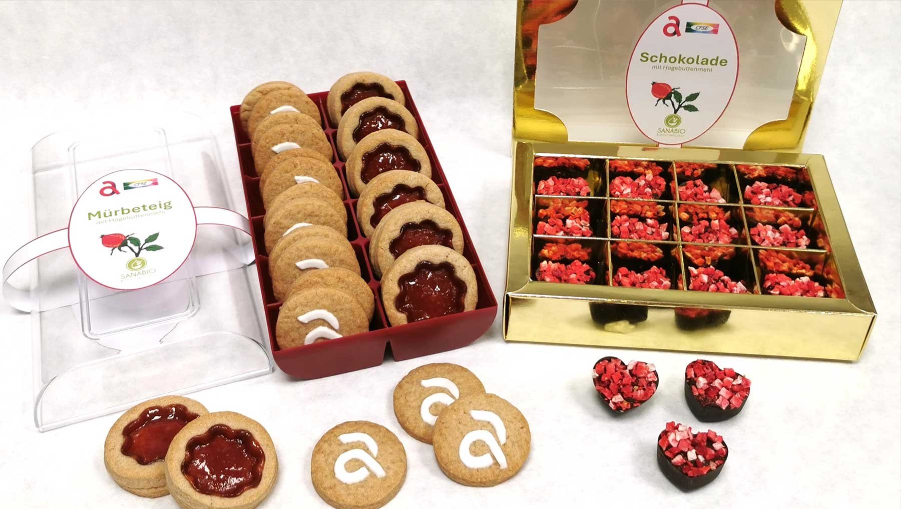 Zwei Geschenkboxen mit Marmeladenteig-Plätzchen und Schokoladen-Himbeer-Desserts: eine Box mit Himbeer-Marmeladenteig-Plätzchen, die andere mit kleinen Schokoladen-Himbeer-Kugeln in goldener Verpackung.