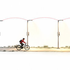 A cyclist rides to the right along a path illuminated ahead by connected streetlights.