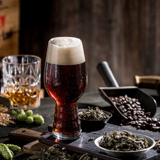 eine Abbildung von handgebrautem, dunklen Bier in einem Glas mit Schaumkrone. Im Vordergrund sind verschiedene Zutaten wie Hopfenpellets, -blüten und gehackte Kaffeebohnen zu sehen, typisch für Craft-Biere. Historische Brautboldsymbolchen verzieren den Hintergrund.

(Kurzbeschreibung für screenreader, ca. 38 Wörter)
