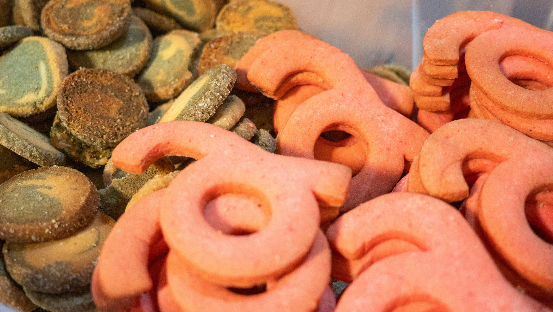 Bunte, spiralförmige und runde Teigstücke, vermutlich frisch gebacken, in verschiedenen Brauntönen und einer leuchtend orangefarbenen Variante, die wie Brezeln geformt sind.