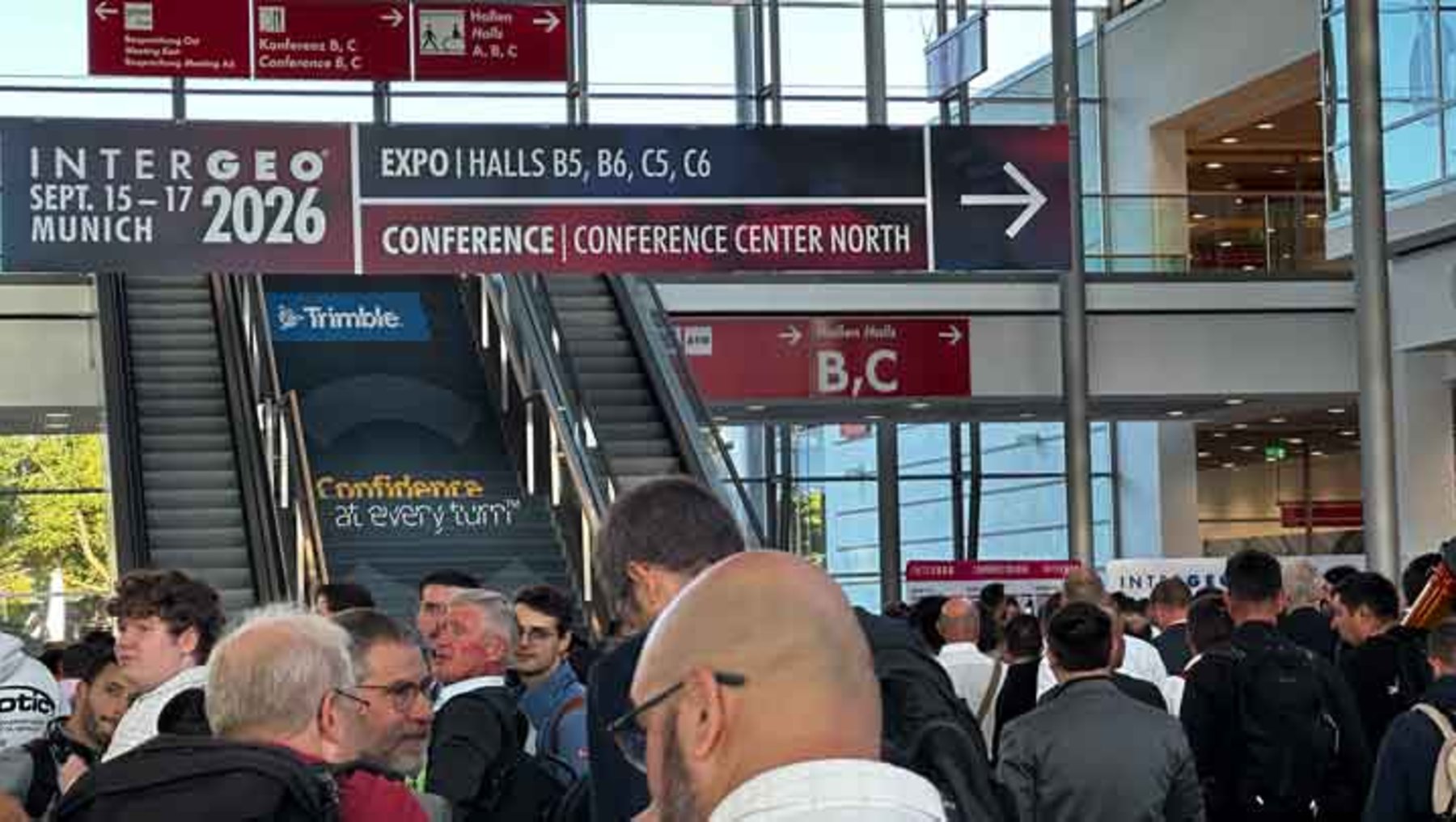 Menschenmenge betritt die INTERGEO-Messe 2026 in München, Halle B5, B6, C5, C6. Treppenaufgang mit Hinweisschildern zu Konferenzzentrum Nord. Viele Besucher in Bewegung, Messeatmosphäre.