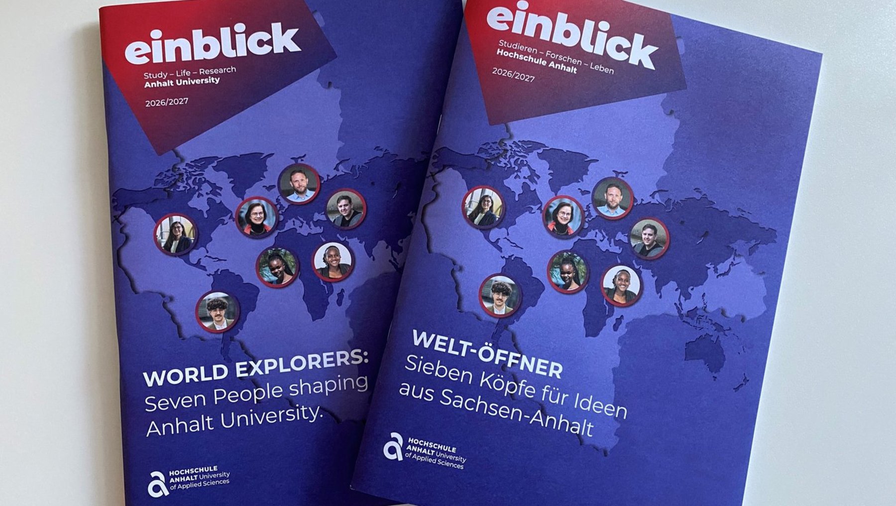Zwei Magazine mit dem Titel „einblick“ der Anhalt University, Jahrgang 2016/2017, zeigen auf dunkelblauem Hintergrund eine Weltkarte mit Porträts von sieben Personen. Links steht „World Explorers: Seven People shaping Anhalt University“, rechts „Welt-Öffner: Sieben Köpfe für Ideen aus Sachsen-Anhalt“.