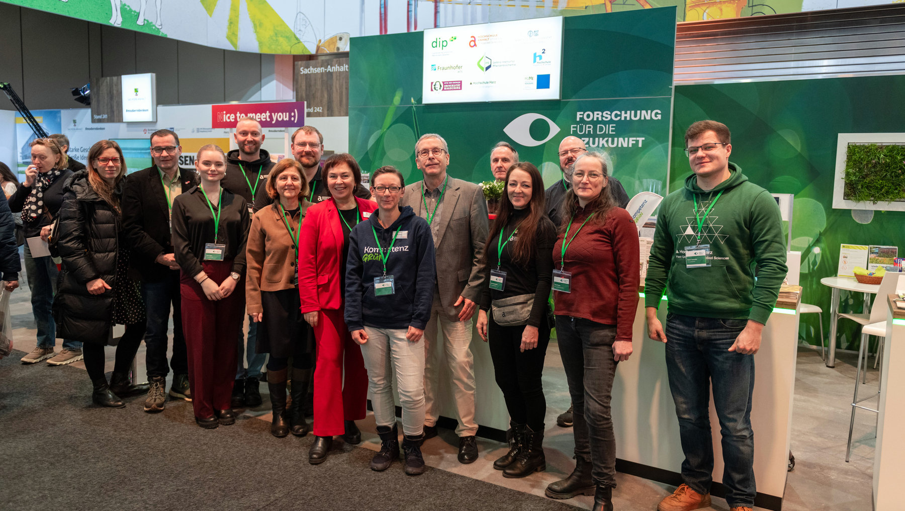 Gruppe von 14 Personen, darunter Wissenschaftler und Forschende, steht lächelnd vor einem Messestand mit dem Schriftzug „Forschung für die Zukunft“ und verschiedenen Logos wie dip, Fraunhofer und Sachsen-Anhalt. Sie tragen Namensschilder und stehen auf einer Messe.