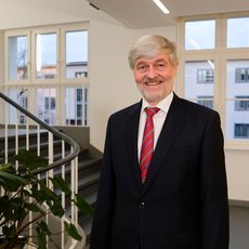 Foto mit freundlich lächelnder Person in einem hellen Raum mit Treppe und großen Fenstern zeigt Prof. Dr. Markus Holz, Vizepräsident für Forschung, Transfer und Nachhaltigkeit der Hochschule Anhalt. 