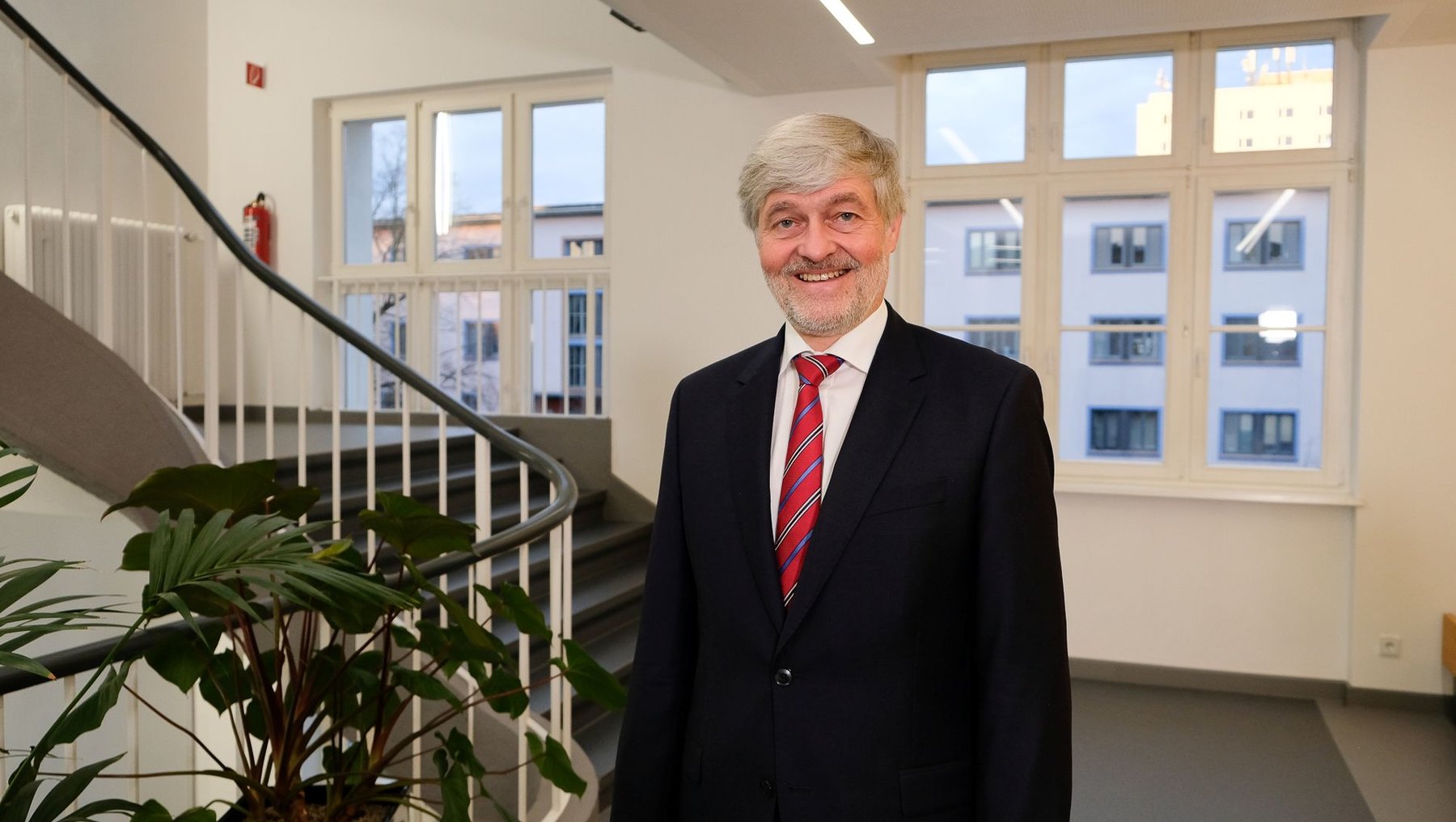 Foto mit freundlich lächelnder Person in einem hellen Raum mit Treppe und großen Fenstern zeigt Prof. Dr. Markus Holz, Vizepräsident für Forschung, Transfer und Nachhaltigkeit der Hochschule Anhalt. 
