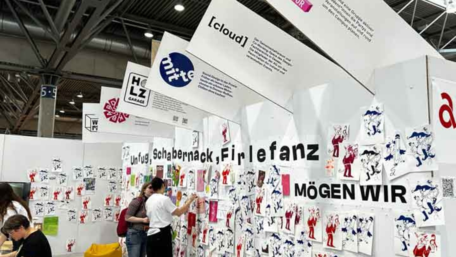 Große Infowand mit vielen bunten, cartoonartigen Zeichnungen von Menschen beim Eislaufen, umgeben von den Texten „Schabernack Firlefanz“, „Mögen WIR“ und dem Logo „[cloud]“. Zwei Personen hängen eine neue Zeichnung an die Wand.
