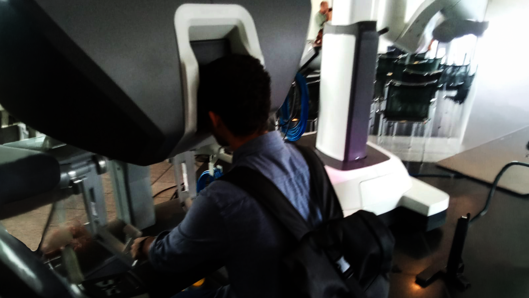 Ein Mensch sitzt in einem medizinischen Gerät, vermutlich einem CT- oder MRT-Scanner, und wird für eine Untersuchung vorbereitet. Der Kopf ist in einer Halterung fixiert, während die Hände auf einer Steuerkonsole liegen.