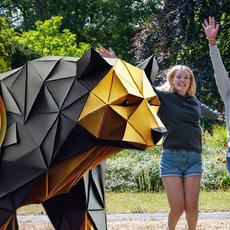 Vier fröhliche Menschen springen mit erhobenen Armen vor einer großen, geometrischen Skulptur aus Metall, die an eine Rakete erinnert. Im Hintergrund ist ein Schild mit den Daten „05.–07. Juni 2026“ und dem Hashtag „#sat2026“ zu sehen.