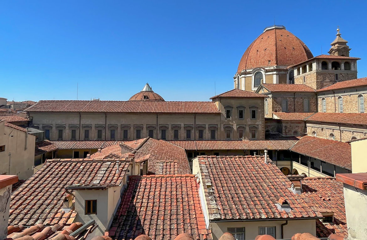 Historische Dachlandschaft der Innenstadt von Florenz mit roten Ziegeldächern, im Hintergrund die Biblioteca Laurenziana und die große Kuppel der Fürstengruft der Medici an der Kirche San Lorenzo. Typisch für italienische Renaissance-Architektur.
