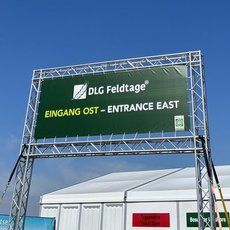 Grüner Schilderaufbau mit weißer Schrift: „DLG Feldtage“ und „Eingang Ost – Entrance East“ vor blauem Himmel, markiert den Ost-Eingang einer Messe oder Veranstaltung.
