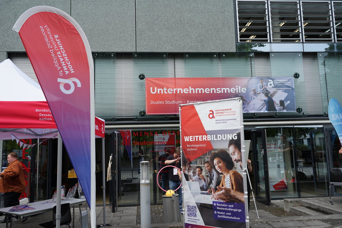 Ein Messeauftritt mit Infostand zur Unternehmensmeile, darunter ein Plakat für Weiterbildung mit dem Fokus auf „Duales Studium“ und „Ausbildung“. Eine Person ist auf dem Plakat beim Lernen mit Tablet zu sehen.